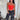 Woman wearing a red strapless top and black pants standing against a white curtain.