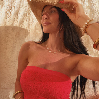 Woman wearing a red strapless top and straw hat against a textured beige wall.